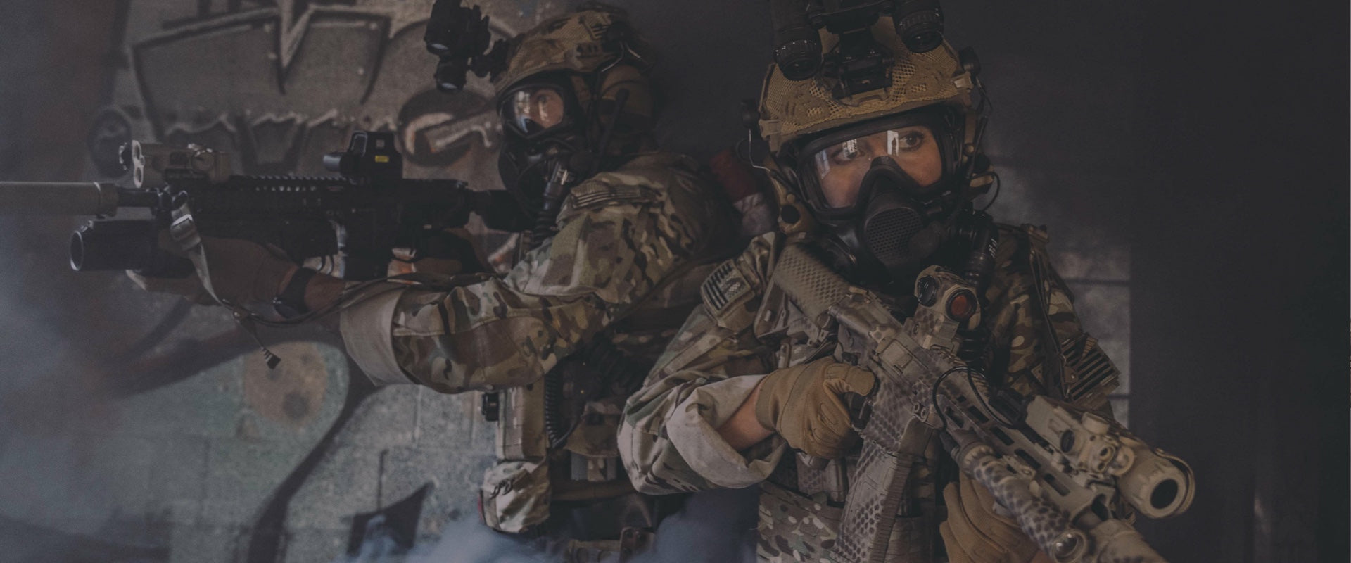 Two soldiers in gas masks and camouflage gear with weapons in a dark setting
